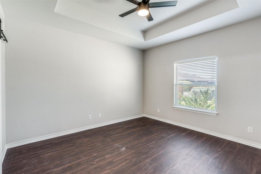 Unfurnished room featuring a tray ceiling, dark wood-type flooring, and ceiling fan Unfurnished room featuring a tray ceiling, dark wood-type flooring, and ceiling fan