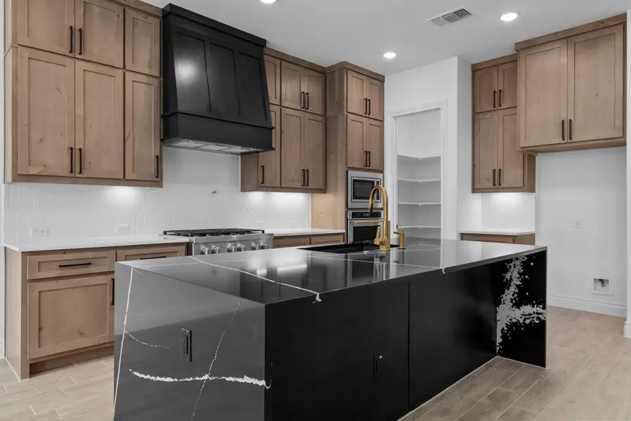 Stylish kitchen with warm wood cabinetry, striking black island with waterfall edge, and high-end stainless steel appliances.
