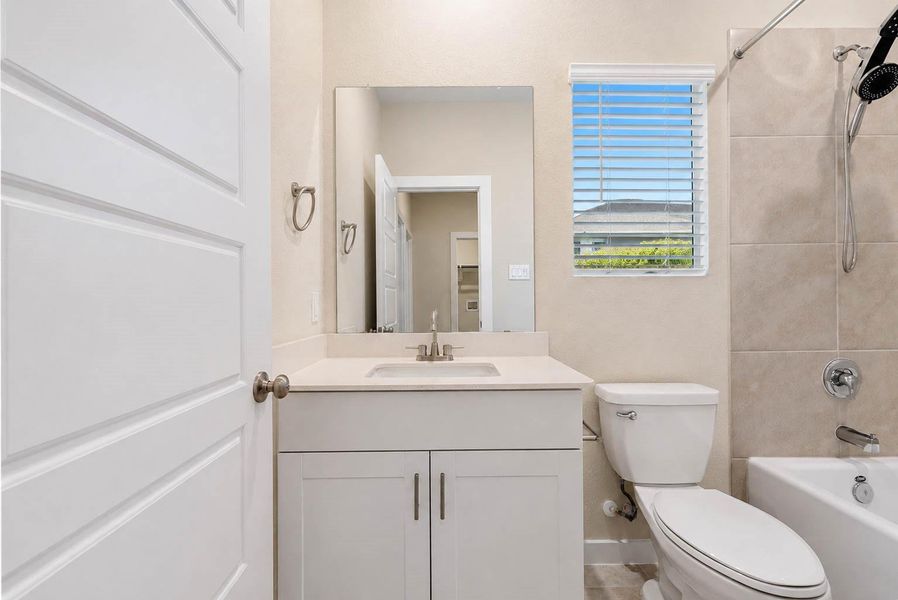 Full secondary bathroom features a sleek white vanity with modern hardware, expansive mirror, window for natural light, and a tiled tub-and-shower combination. Neutral finishes and clean lines create a fresh, functional space with practical storage and an easy-care design. Full secondary bathroom features a sleek white vanity with modern hardware, expansive mirror, window for natural light, and a tiled tub-and-shower combination. Neutral finishes and clean lines create a fresh, functional space with practical storage and an easy-care design.