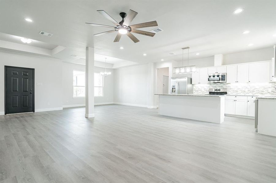 Unfurnished living room with ceiling fan with notable chandelier, light wood-type flooring, and a tray ceiling