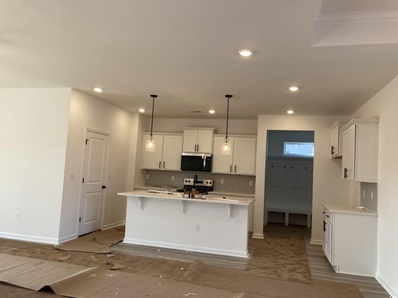 Kitchen with hanging light fixtures, a kitchen island with sink, a breakfast bar, decorative backsplash, and white cabinets Kitchen with hanging light fixtures, a kitchen island with sink, a breakfast bar, decorative backsplash, and white cabinets