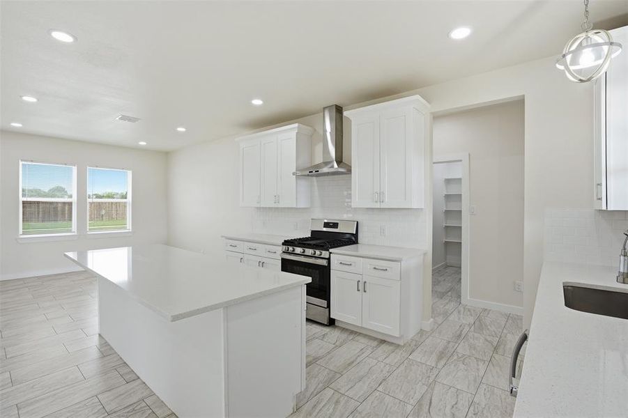 Contemporary kitchen featuring a large central island with a solid surface countertop, white cabinetry, stainless steel range with overhead hood, and light-toned tile flooring