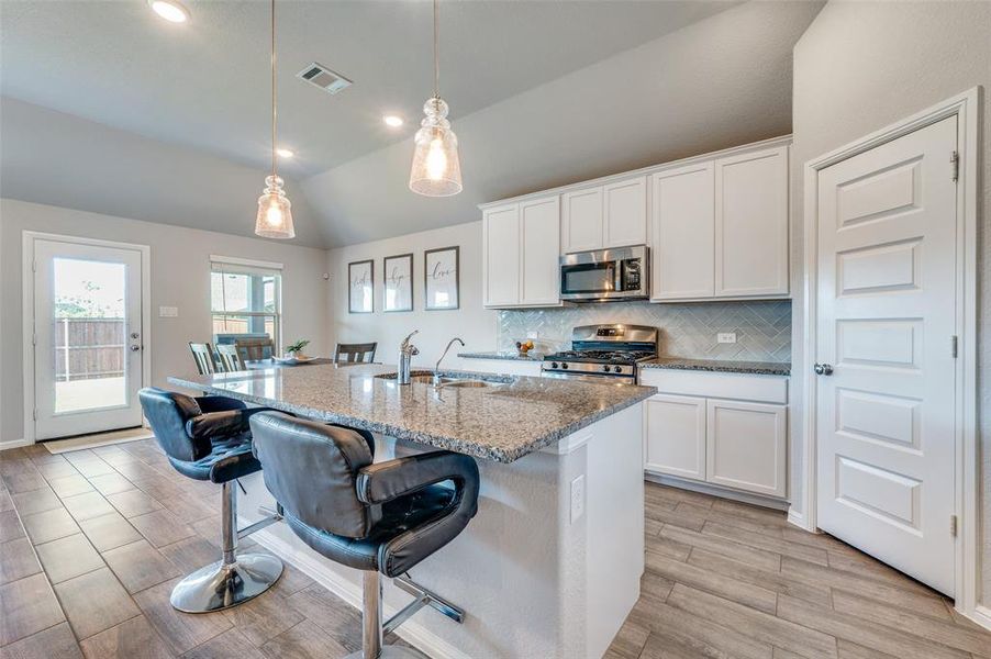 Kitchen featuring a breakfast bar, appliances with stainless steel finishes, vaulted ceiling, backsplash, and white cabinetry Kitchen featuring a breakfast bar, appliances with stainless steel finishes, vaulted ceiling, backsplash, and white cabinetry
