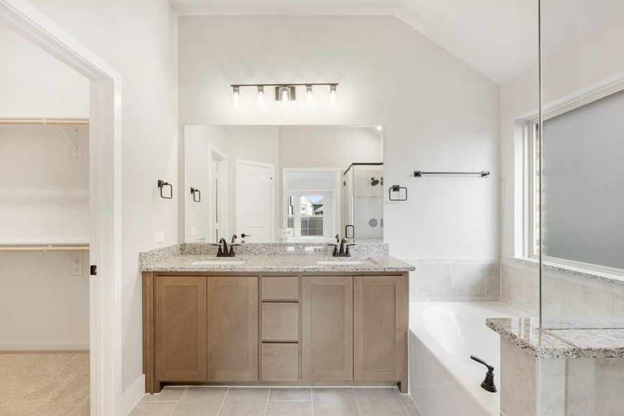 Master bathroom with double vanity, granite countertops, soaking tub, and walk-in closet access