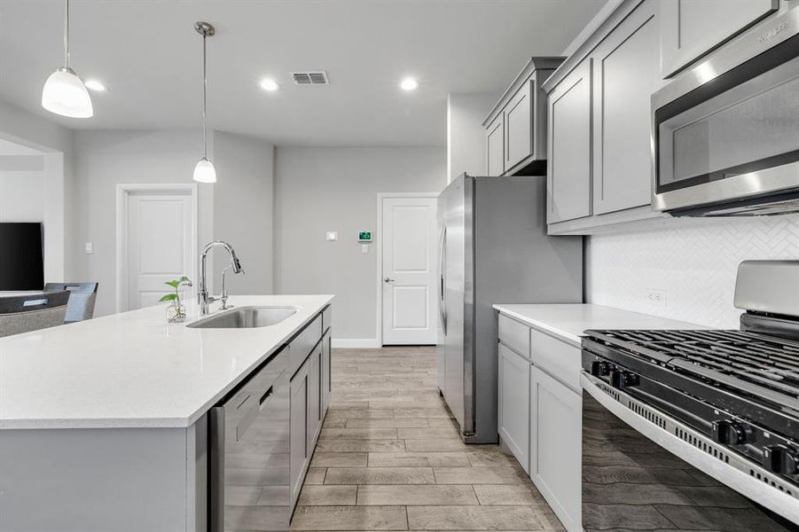 Kitchen with stainless steel appliances, light countertops, light wood-style flooring, decorative light fixtures, and tasteful backsplash