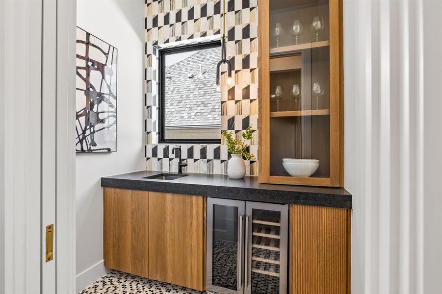 Indoor wet bar with beverage cooler, glass insert cabinets, brown cabinets, backsplash, and dark stone countertops Indoor wet bar with beverage cooler, glass insert cabinets, brown cabinets, backsplash, and dark stone countertops
