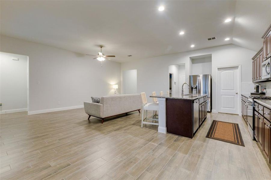 Kitchen featuring light stone counters, an island with sink, light hardwood / wood-style floors, dark brown cabinets, and appliances with stainless steel finishes