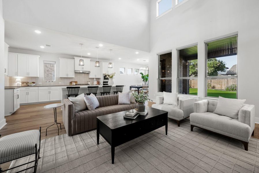 A spacious, open-concept design connects the well-lit kitchen and living area, featuring soaring ceilings and tall windows.