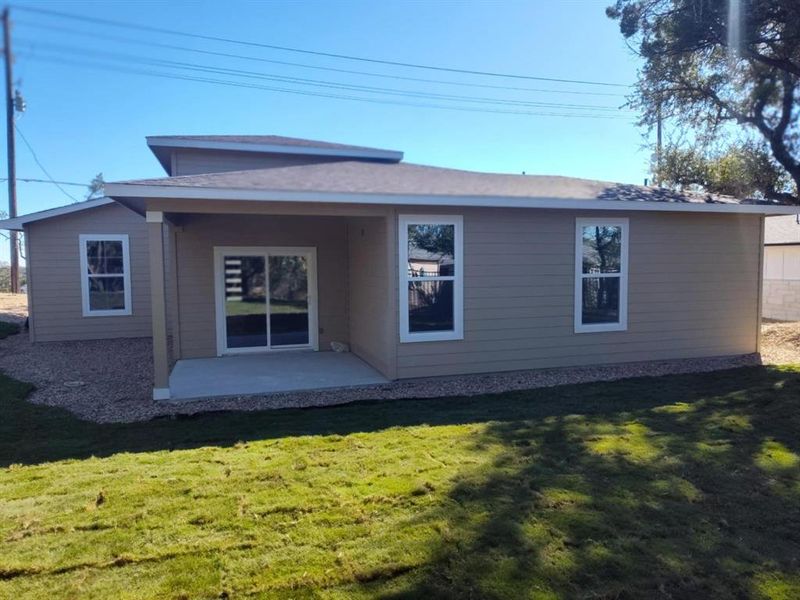Rear view of property featuring a patio area, a yard, and a shingled roof Rear view of property featuring a patio area, a yard, and a shingled roof