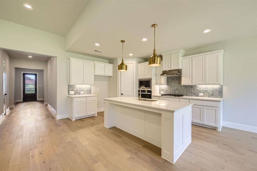 Kitchen with backsplash, white cabinetry, a center island with sink, light wood-type flooring, and recessed lighting Kitchen with backsplash, white cabinetry, a center island with sink, light wood-type flooring, and recessed lighting