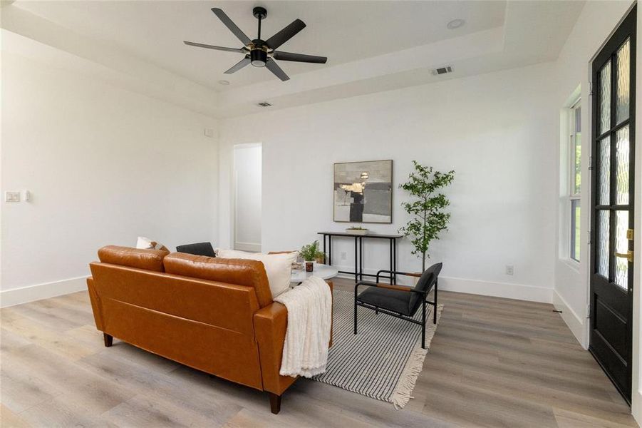 Living room featuring ceiling fan, light wood-type flooring, and a tray ceiling