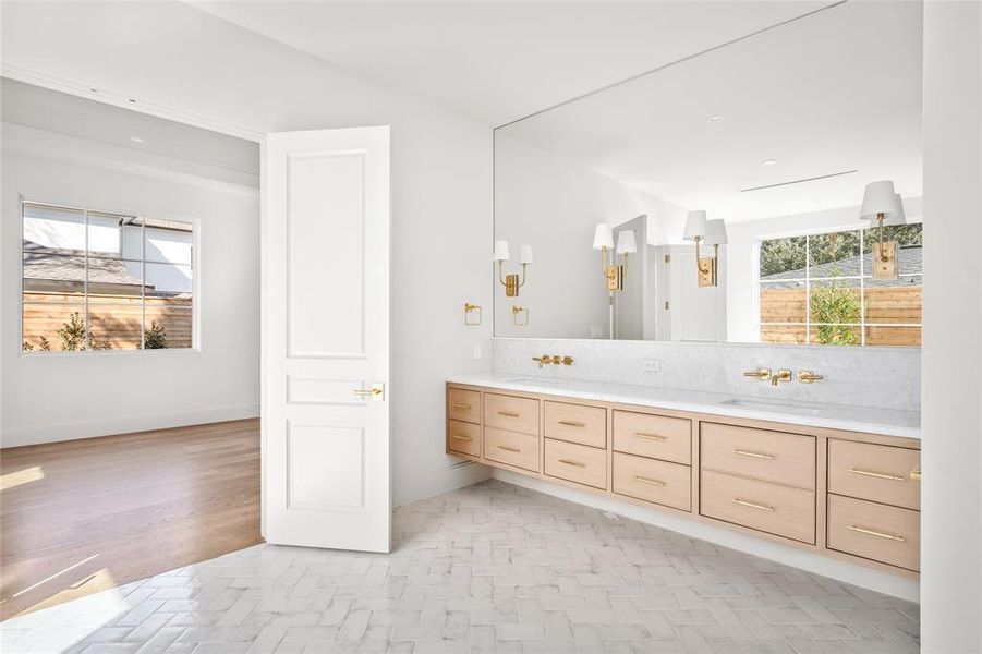 the ensuite bathroom for the second primary suite features an Opal White marble dual vanity complemented by refined Signature Hardware brass pulls. Thomas O’Brien sconces add a touch of designer sophistication, while a textured subway tile floor enhances the space with subtle depth. A private water closet offers added convenience, and direct access to a spacious walk-in closet ensures seamless organization.