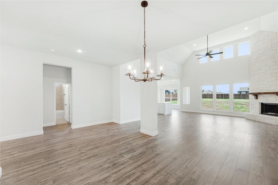 Open living and dining area with vaulted ceiling, wood floors, chandelier, and stone fireplace