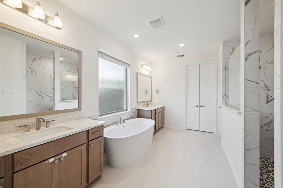 The luxury primary bath offers a spa-like experience with dual vanities, a deep soaking tub, and an oversized marble-style shower. A spacious walk-in closet completes the retreat, blending elegance with everyday functionality.