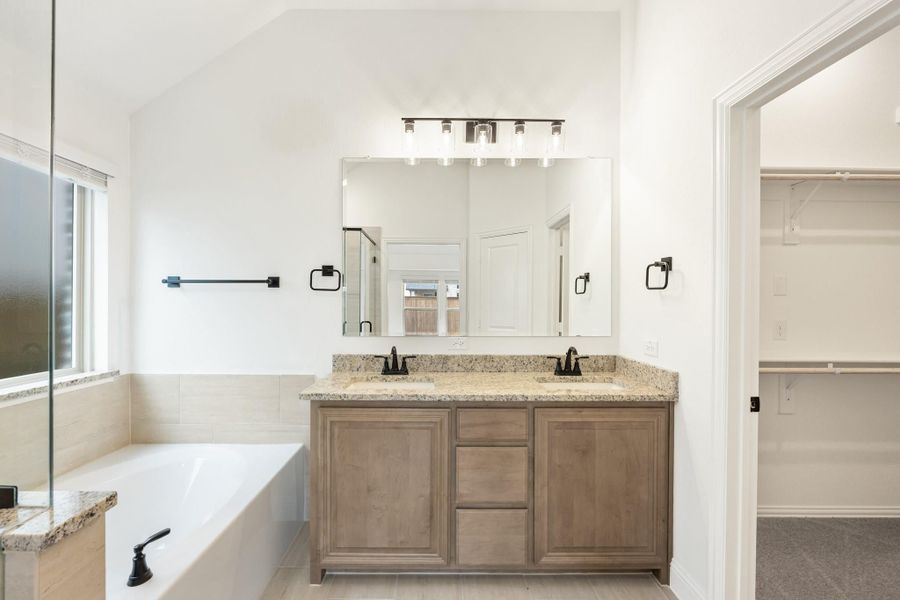 Master bathroom with double sink vanity, granite countertop, soaking tub, and walk-in closet entrance Master bathroom with double sink vanity, granite countertop, soaking tub, and walk-in closet entrance