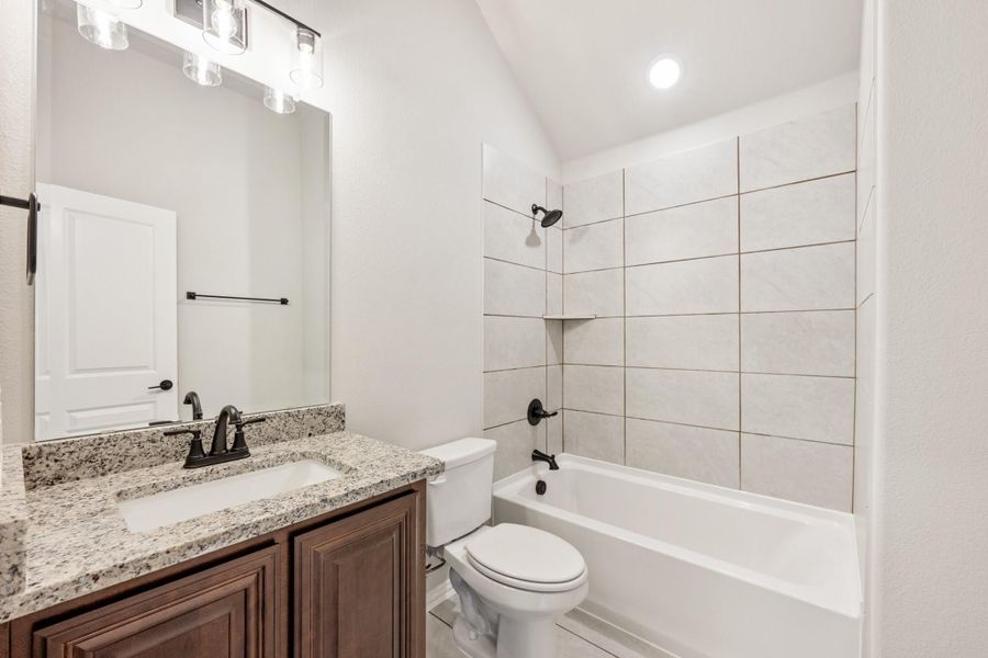 Bathroom with granite vanity, dark wood cabinets, toilet, and tiled shower-tub combo with vaulted ceiling Bathroom with granite vanity, dark wood cabinets, toilet, and tiled shower-tub combo with vaulted ceiling