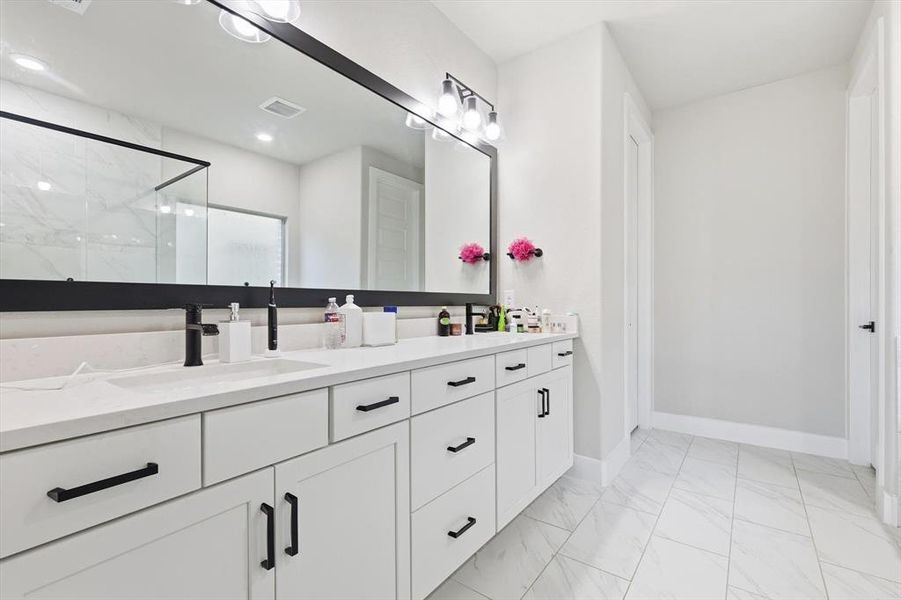 Full bath featuring a marble finish shower, double vanity, and light marble finish floors