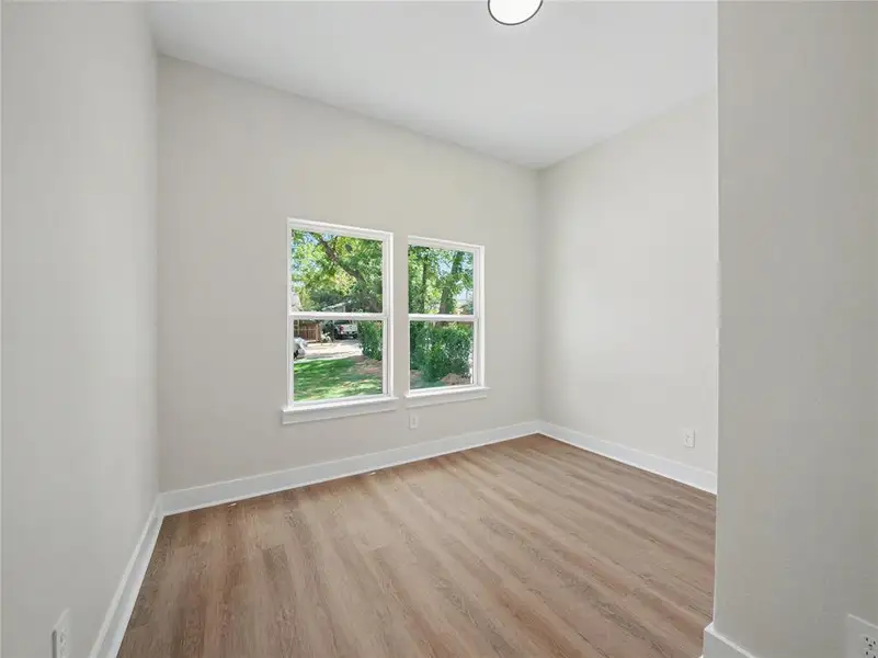 Bright interior room featuring a neutral color palette, wood-finish flooring, two window openings with white trim, and a ceiling-mounted light fixture Bright interior room featuring a neutral color palette, wood-finish flooring, two window openings with white trim, and a ceiling-mounted light fixture