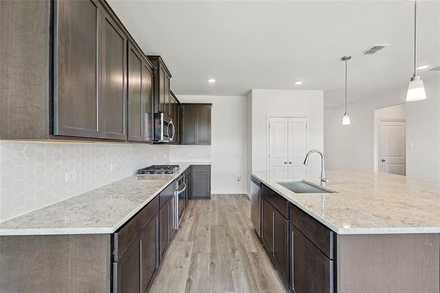 Kitchen with hanging light fixtures, sink, light hardwood / wood-style floors, appliances with stainless steel finishes, and backsplash