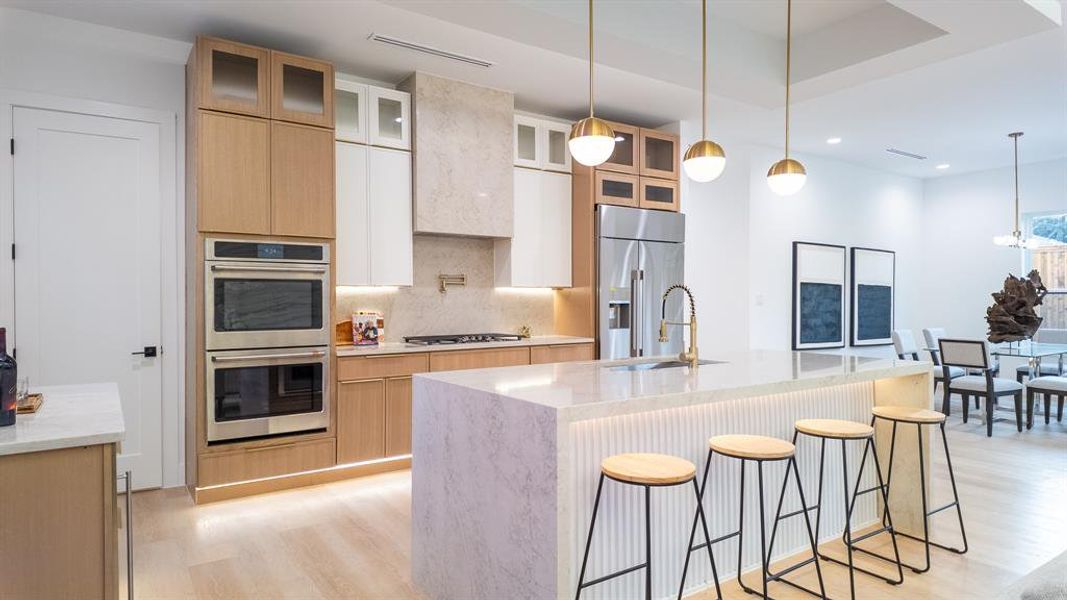 Kitchen with light stone counters,Taj Mahal quartz countertops, light brown cabinets, light wood-style flooring, a breakfast bar, and stainless steel appliances