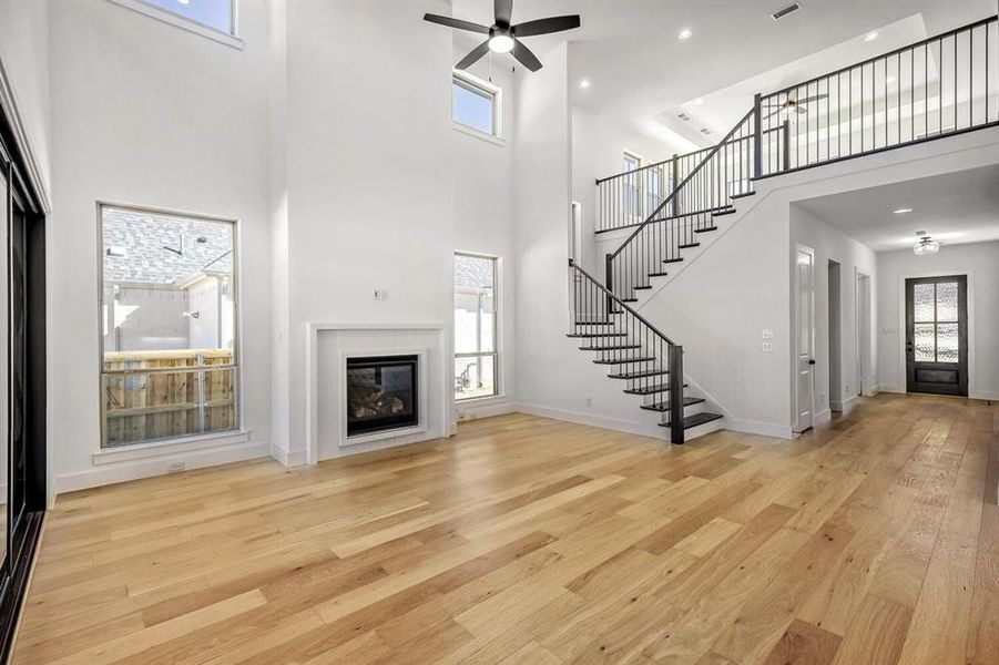Unfurnished living room with a ceiling fan, light wood-style flooring, a glass covered fireplace, a high ceiling, and recessed lighting