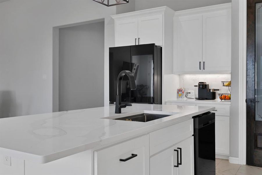 Kitchen featuring black dishwasher, a center island with sink, light stone counters, marble look floor tile, and a sink