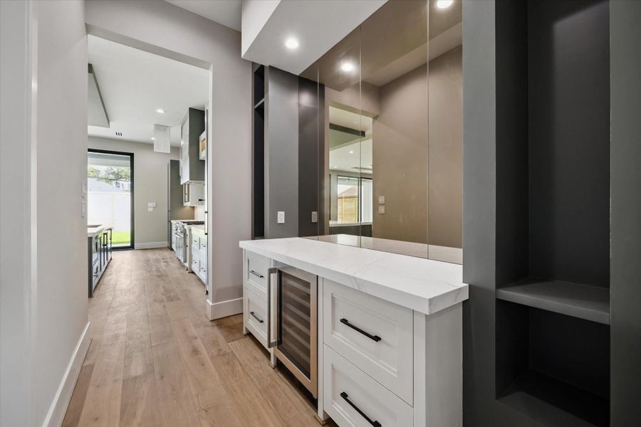 The butler’s pantry bar area is both stylish and functional, highlighted by an antiqued mirrored wall that adds depth and sophistication. Inset shelving provides elegant display space, while a sleek quartz buffet with a built-in wine cooler and four drawers offers ample storage and convenience for entertaining.