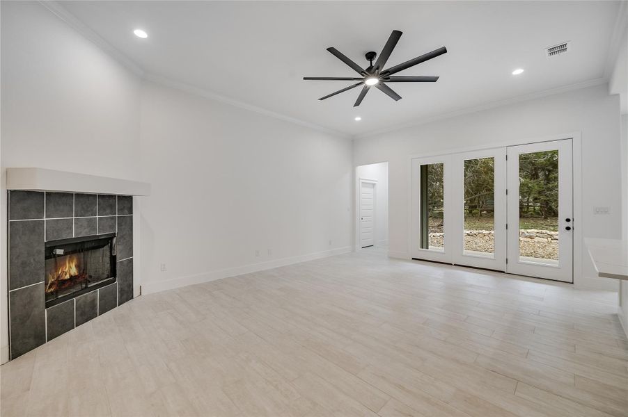 Unfurnished living room featuring ornamental molding, visible vents, a tiled fireplace, and wood finished floors