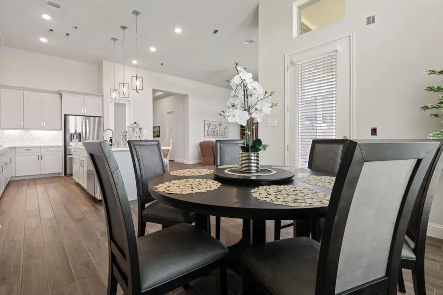 This photo showcases a modern, open-concept dining and kitchen area. The space features sleek cabinetry, stainless steel appliances, and elegant lighting. The dining table is set with decorative placemats and a floral centerpiece, complemented by wood flooring and ample natural light. This photo showcases a modern, open-concept dining and kitchen area. The space features sleek cabinetry, stainless steel appliances, and elegant lighting. The dining table is set with decorative placemats and a floral centerpiece, complemented by wood flooring and ample natural light.