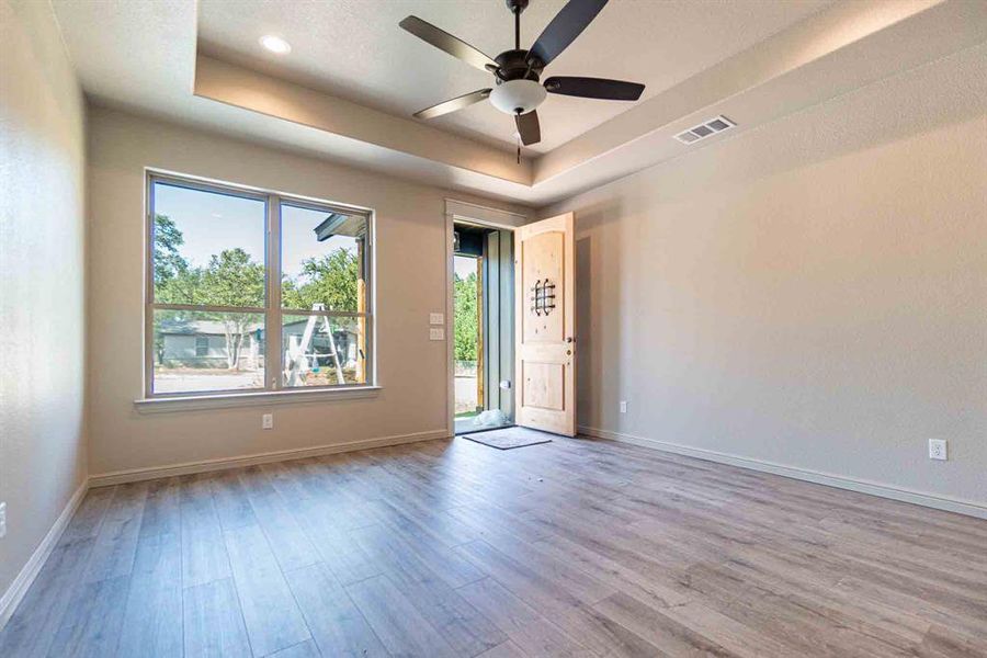 Spare room featuring a tray ceiling, light wood-style flooring, and ceiling fan