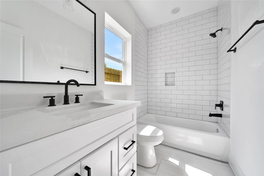 This modern bathroom features a sleek design with white subway tiles, a spacious vanity with black fixtures, and a large mirror. The natural light from the window enhances the clean, bright atmosphere.