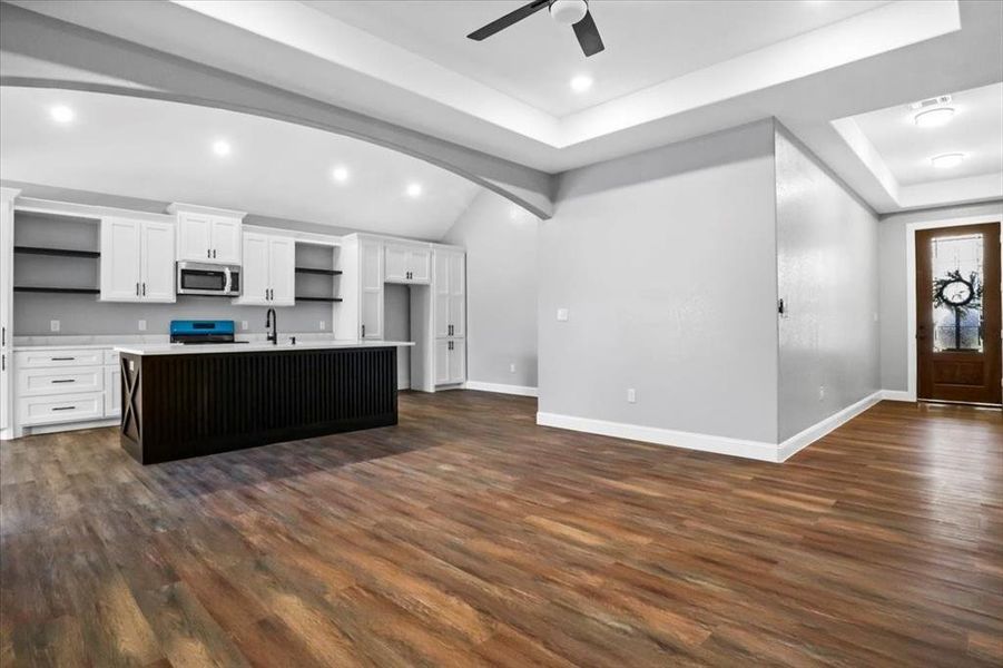 Kitchen featuring sink, dark wood-type flooring, a center island with sink, white cabinets, and range