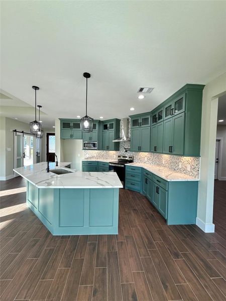 This modern kitchen features teal cabinetry, sleek marble countertops, and a central island with pendant lighting. The wood-look tile flooring adds warmth, while the open layout invites easy movement and entertaining. This modern kitchen features teal cabinetry, sleek marble countertops, and a central island with pendant lighting. The wood-look tile flooring adds warmth, while the open layout invites easy movement and entertaining.