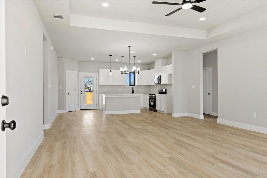Unfurnished living room with light wood finished floors, ceiling fan, a raised ceiling, and suspended lighting