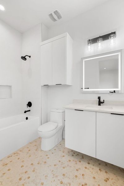 A well-appointed bath features a sleek white vanity and tub, complemented by stylish hex-tile flooring.