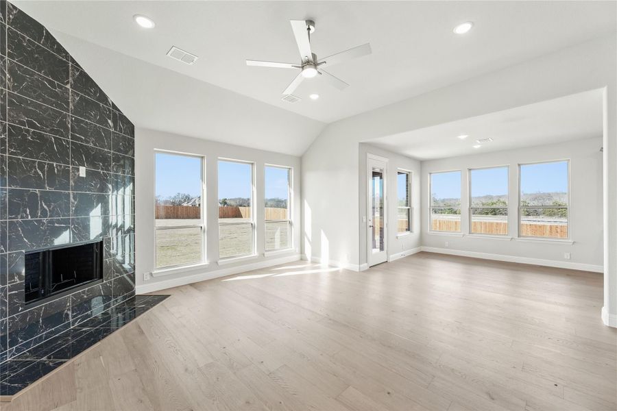 Open living room with dark marble tile fireplace, light hardwood floors, and ceiling fan Open living room with dark marble tile fireplace, light hardwood floors, and ceiling fan