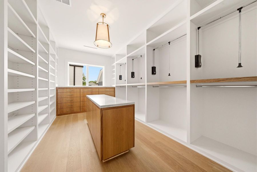 Boutique-style primary closet with center island, custom cabinetry, extensive shelving, and dedicated wardrobe storage. Boutique-style primary closet with center island, custom cabinetry, extensive shelving, and dedicated wardrobe storage.