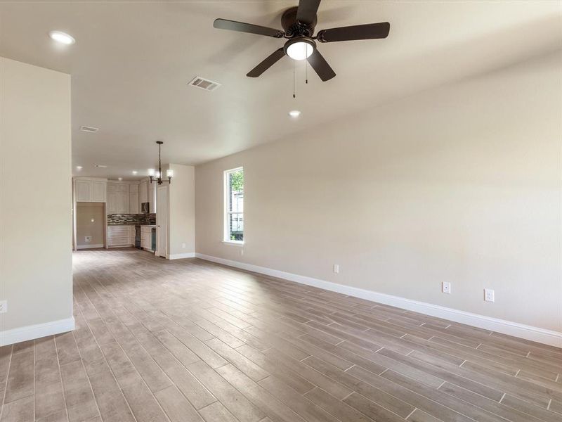Unfurnished living room featuring light wood-style floors, recessed lighting, ceiling fan, and a chandelier Unfurnished living room featuring light wood-style floors, recessed lighting, ceiling fan, and a chandelier