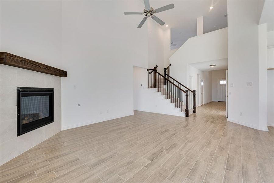 Unfurnished living room with a tiled fireplace, ceiling fan, a high ceiling, and light wood-type flooring