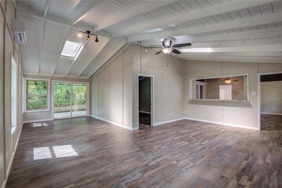 Unfurnished living room with dark hardwood / wood-style flooring, ceiling fan, and vaulted ceiling with skylight