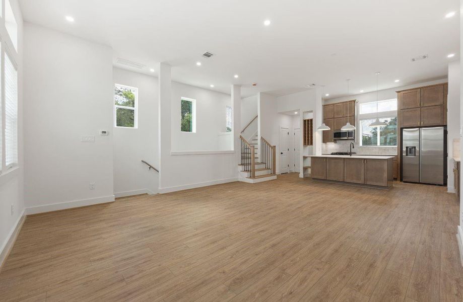 The second-floor living space flows beautifully into the kitchen, combining modern finishes with an open-concept design. Large windows, high ceilings, recessed lighting, and warm flooring give the room a bright, elevated feel, while the kitchen remains connected for easy entertaining.