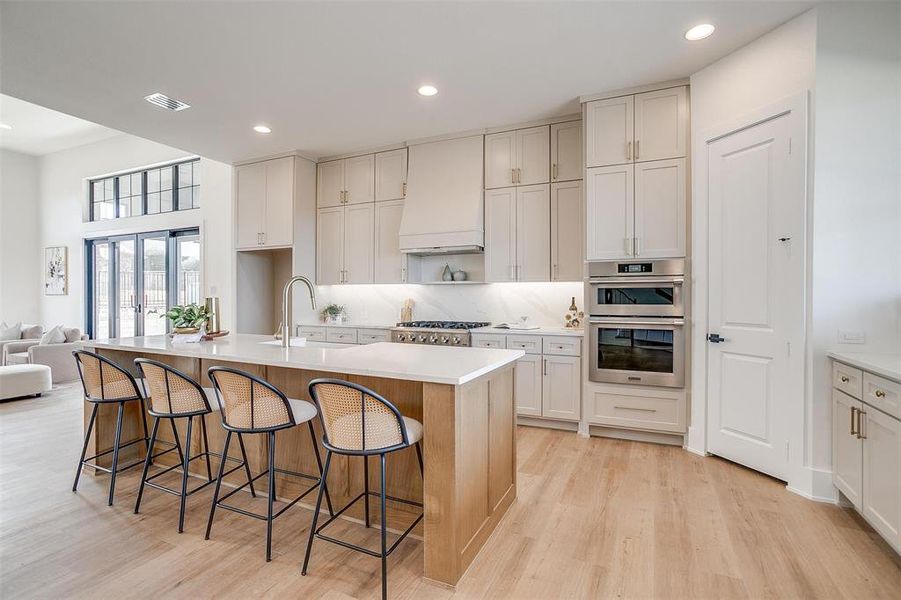 Kitchen featuring premium range hood, light wood-style flooring, a sink, stainless steel appliances, and light countertops