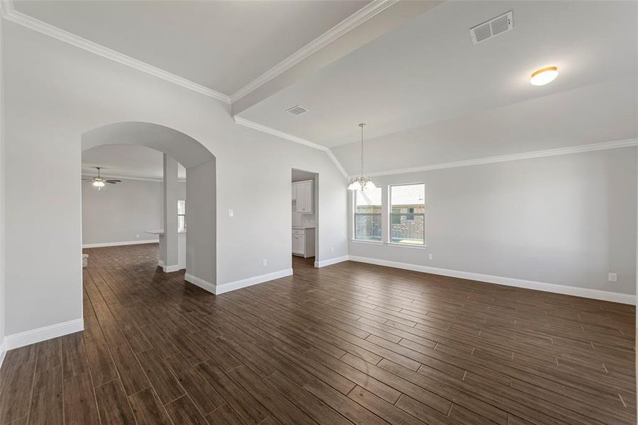 Empty room with ornamental molding, ceiling fan with notable chandelier, and dark wood-type flooring