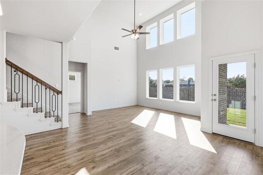 Unfurnished living room featuring healthy amount of natural light, a high ceiling, a ceiling fan, light wood finished floors, and stairs