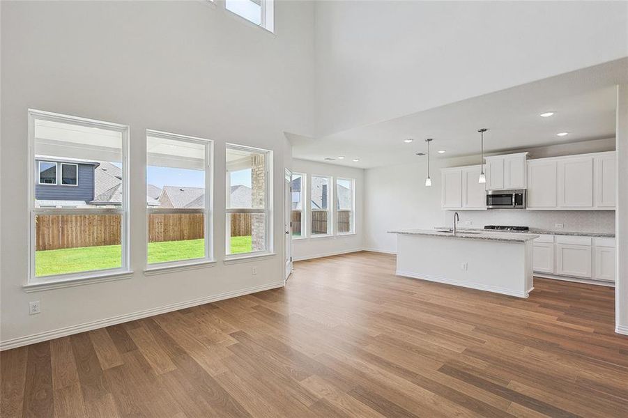 Unfurnished living room featuring sink, light hardwood / wood-style flooring, and a towering ceiling