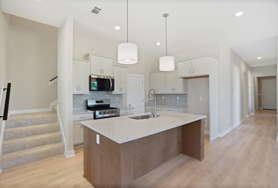 Kitchen featuring stainless steel appliances, an island with sink, light wood finished floors, pendant lighting, and light stone countertops