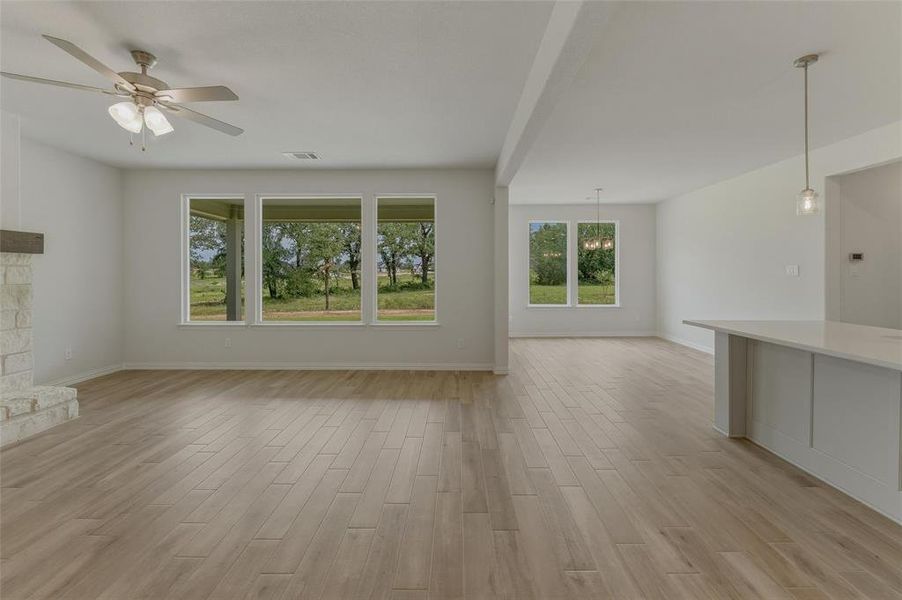 Open-concept living space featuring wood-finish flooring, a stone fireplace with a wood mantle, and a ceiling fan with integrated lighting
