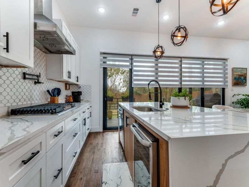Kitchen featuring white cabinets, light stone counters, a center island with sink, wall chimney exhaust hood, and recessed lighting