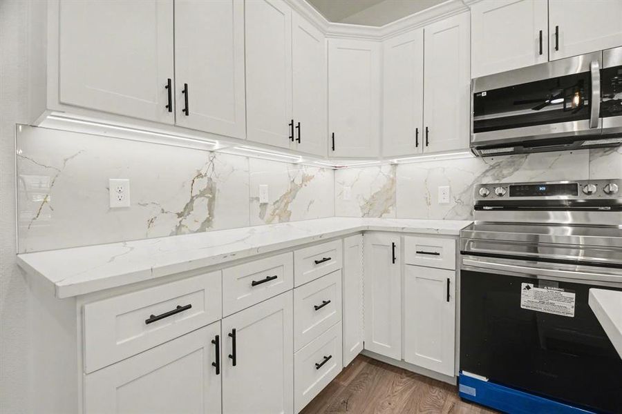 The kitchen features white cabinetry with black hardware, complementing the light-colored countertops and marble-patterned backsplash