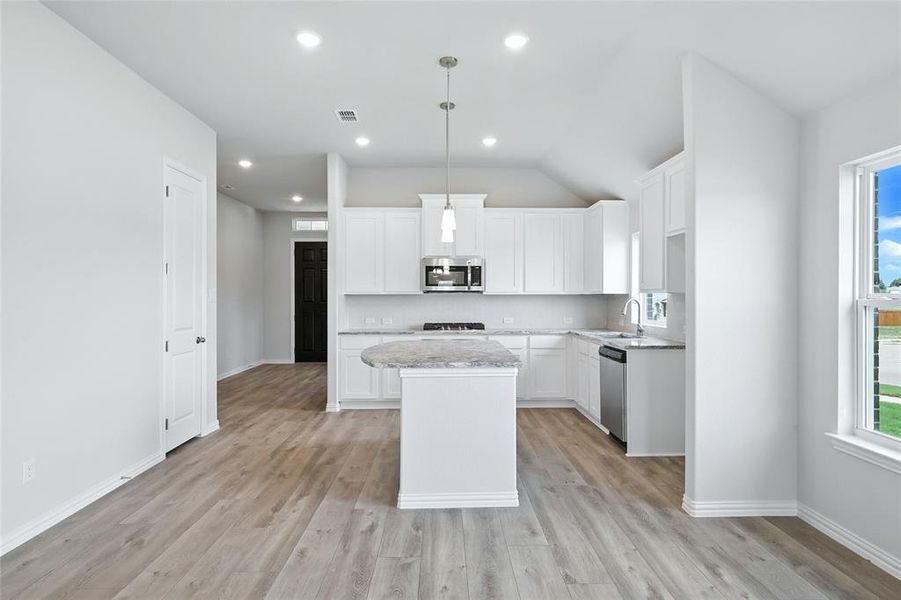 Kitchen with appliances with stainless steel finishes, a kitchen island, light wood-style flooring, white cabinetry, and lofted ceiling